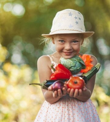 Young girl carrying fresh vegetables in a field with the sun shining