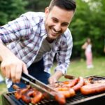 A man smiling while looking meat on the BBQ