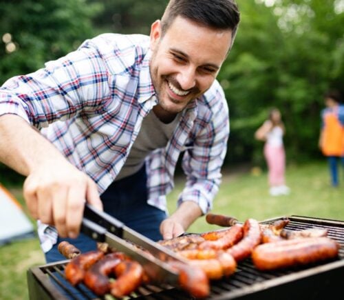 A man smiling while looking meat on the BBQ