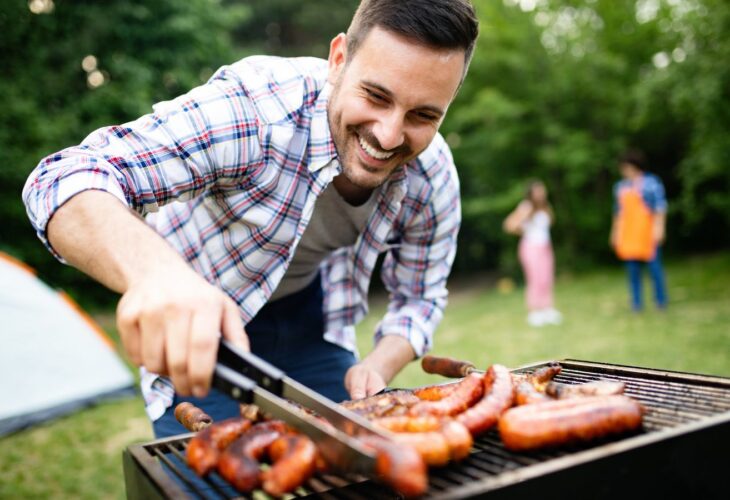 A man smiling while looking meat on the BBQ