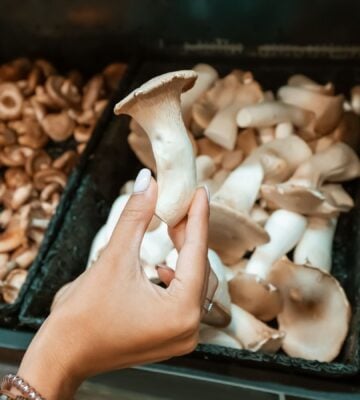 A person in a grocery store holds a king oyster mushroom, which have been growingly popular