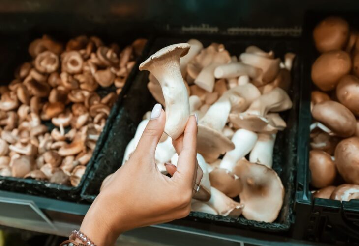 A person in a grocery store holds a king oyster mushroom, which have been growingly popular