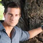 Bear Grylls, owner of an ancestral supplements brand that promotes the benefits of organ meat, resting his hand on a tree