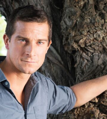 Bear Grylls, owner of an ancestral supplements brand that promotes the benefits of organ meat, resting his hand on a tree