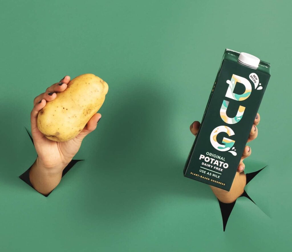 Vegan DUG potato milk next to a potato in front of a green background