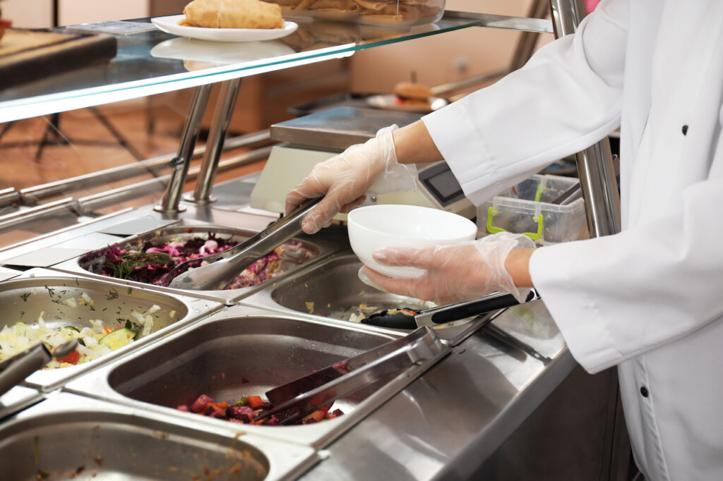 University canteen worker at serving line, with plant-based food