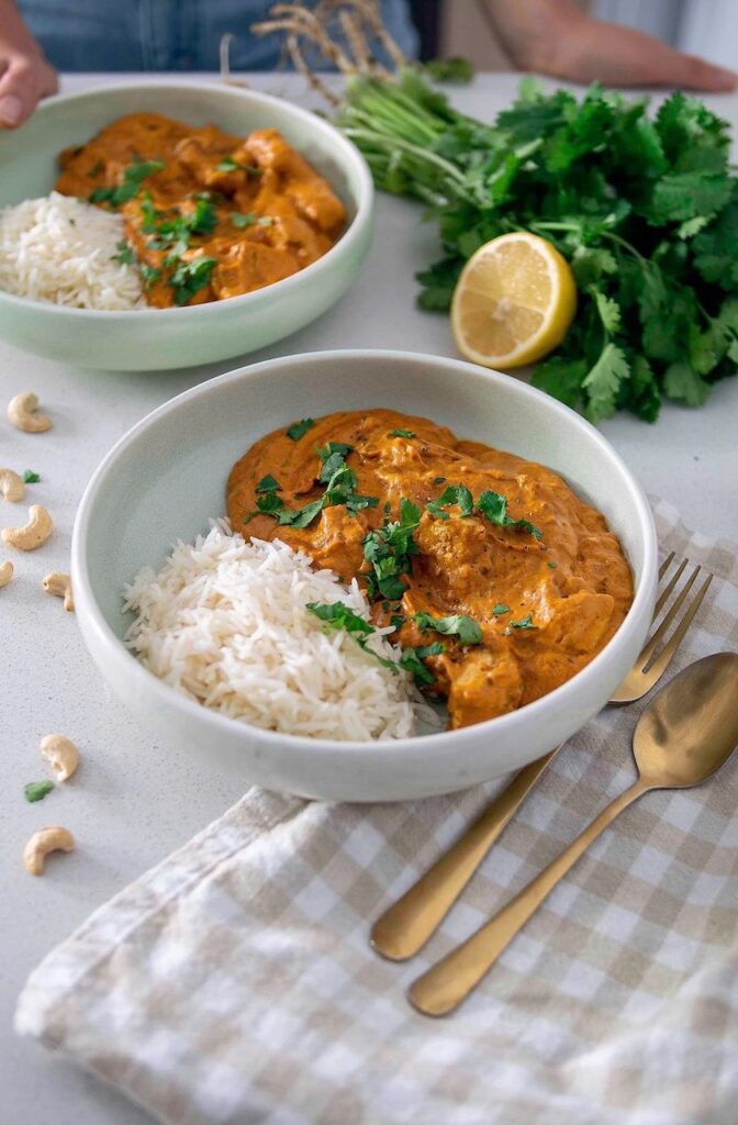 A white bowl full of vegan butter chicken curry and rice with a fresh coriander garnish