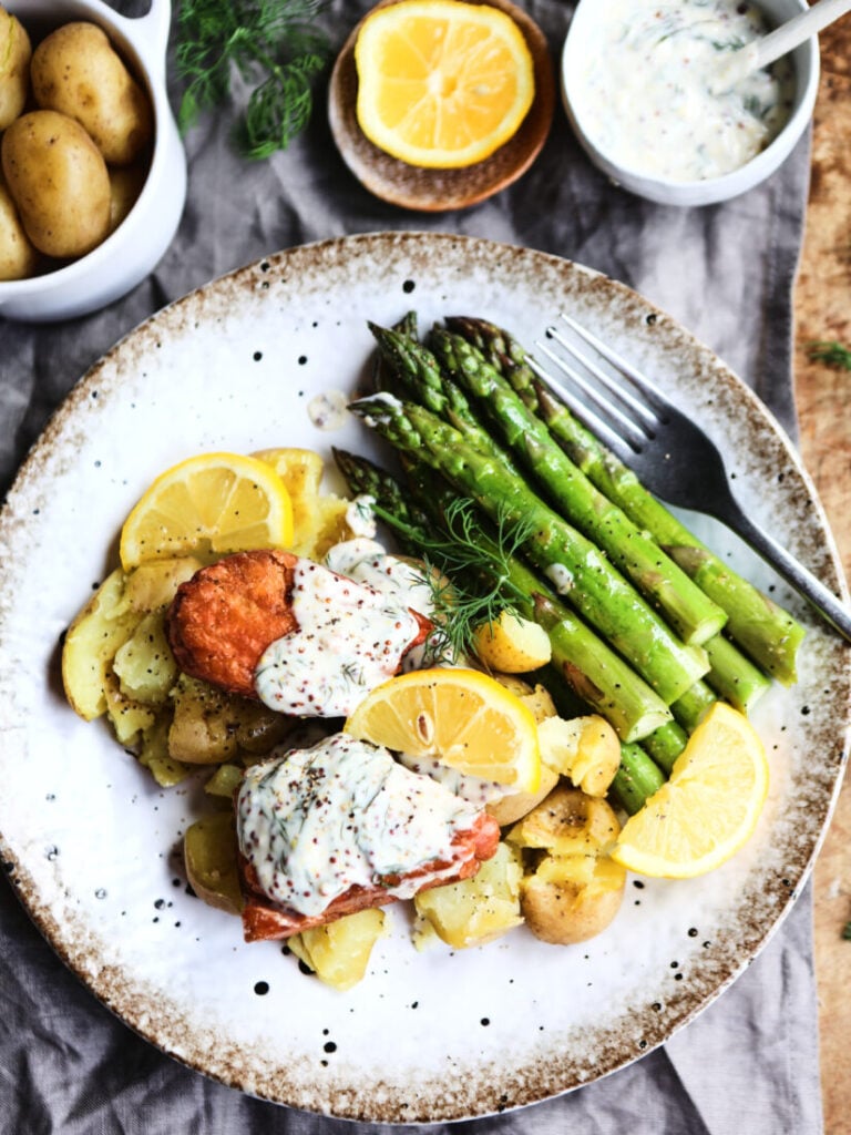 Vegan salmon fillets served with creamy dill sauce and vegetables on a white speckled plate