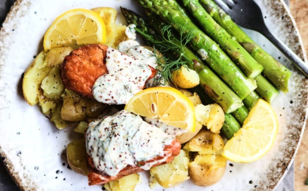 Vegan salmon fillets served with creamy dill sauce and vegetables on a white speckled plate
