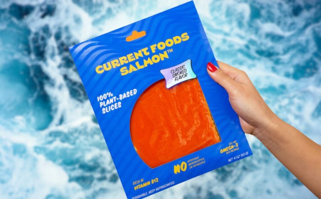 a person's hand holding a packet of vegan salmon made by plant-based seafood brand Current Foods