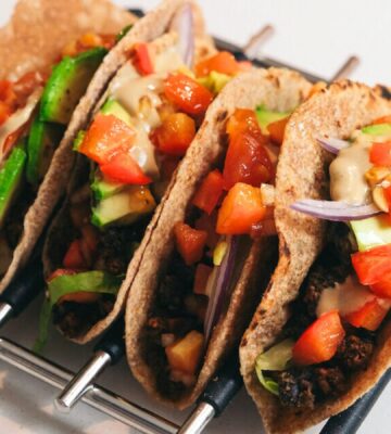 A rack of freshly-stuffed vegan tacos in wholegrain tortilla with creamy tahini dressing on top