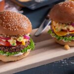 Two fully loaded vegan bean burgers topped with dairy-free mac and cheese and served in bread buns