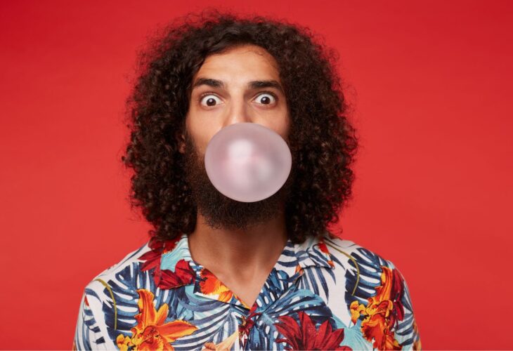A person blowing a bubble with chewing gum on a red background