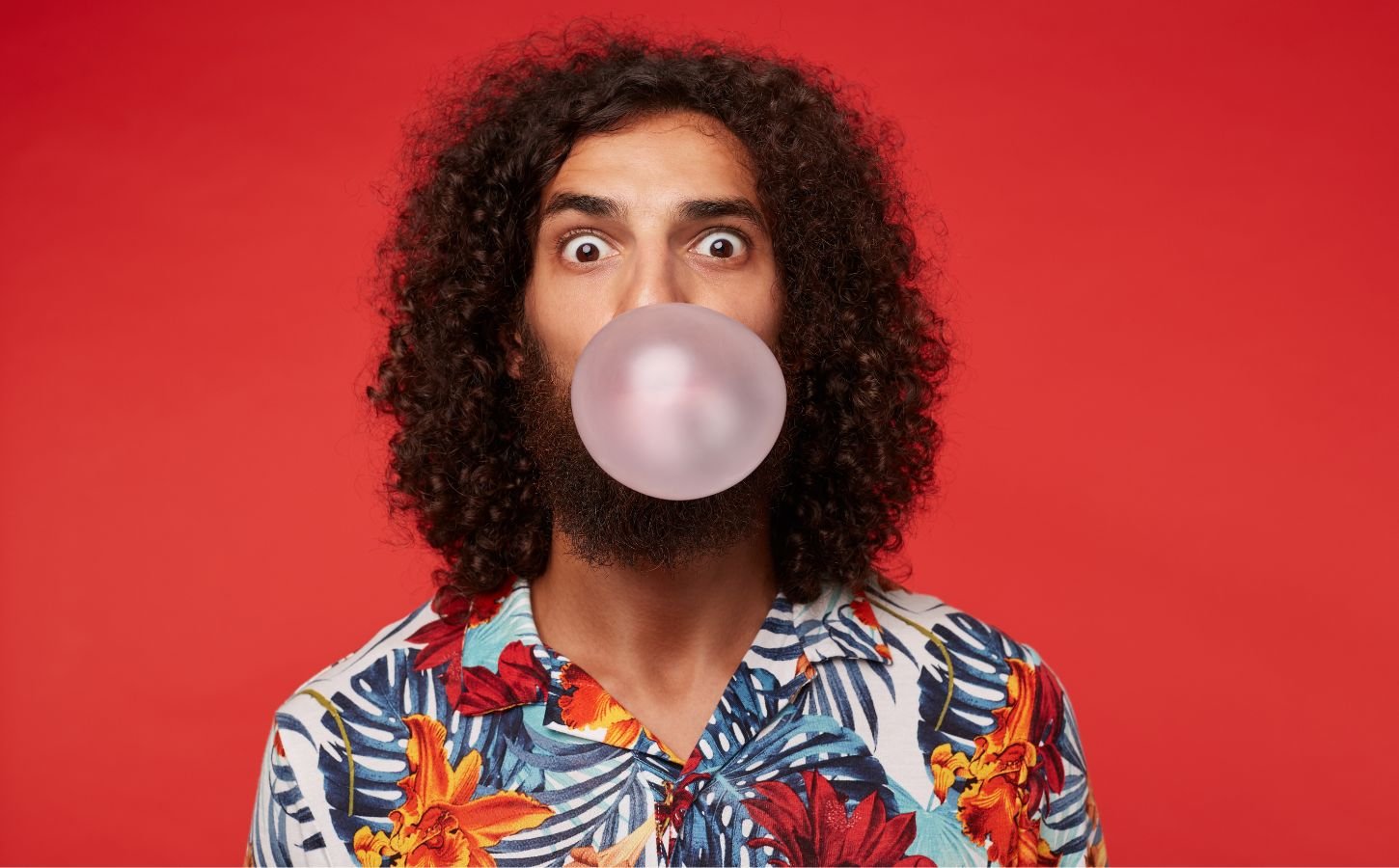 A person blowing a bubble with chewing gum on a red background