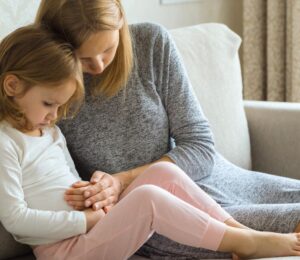 A child with digestive problems being consoled by her mother on the sofa