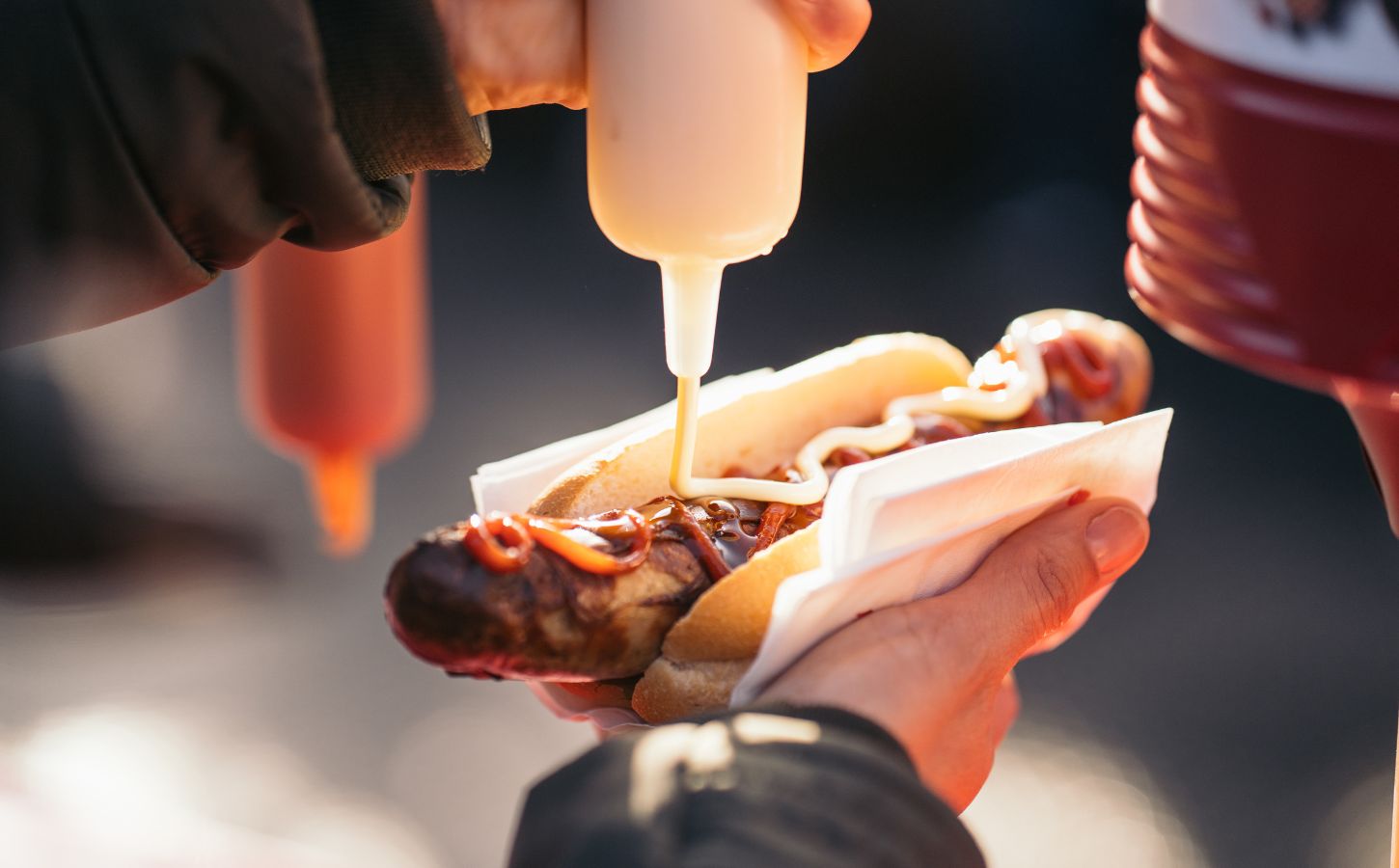 A person's hand squeezing sauce onto a meat hot dog, which can raise stroke risk