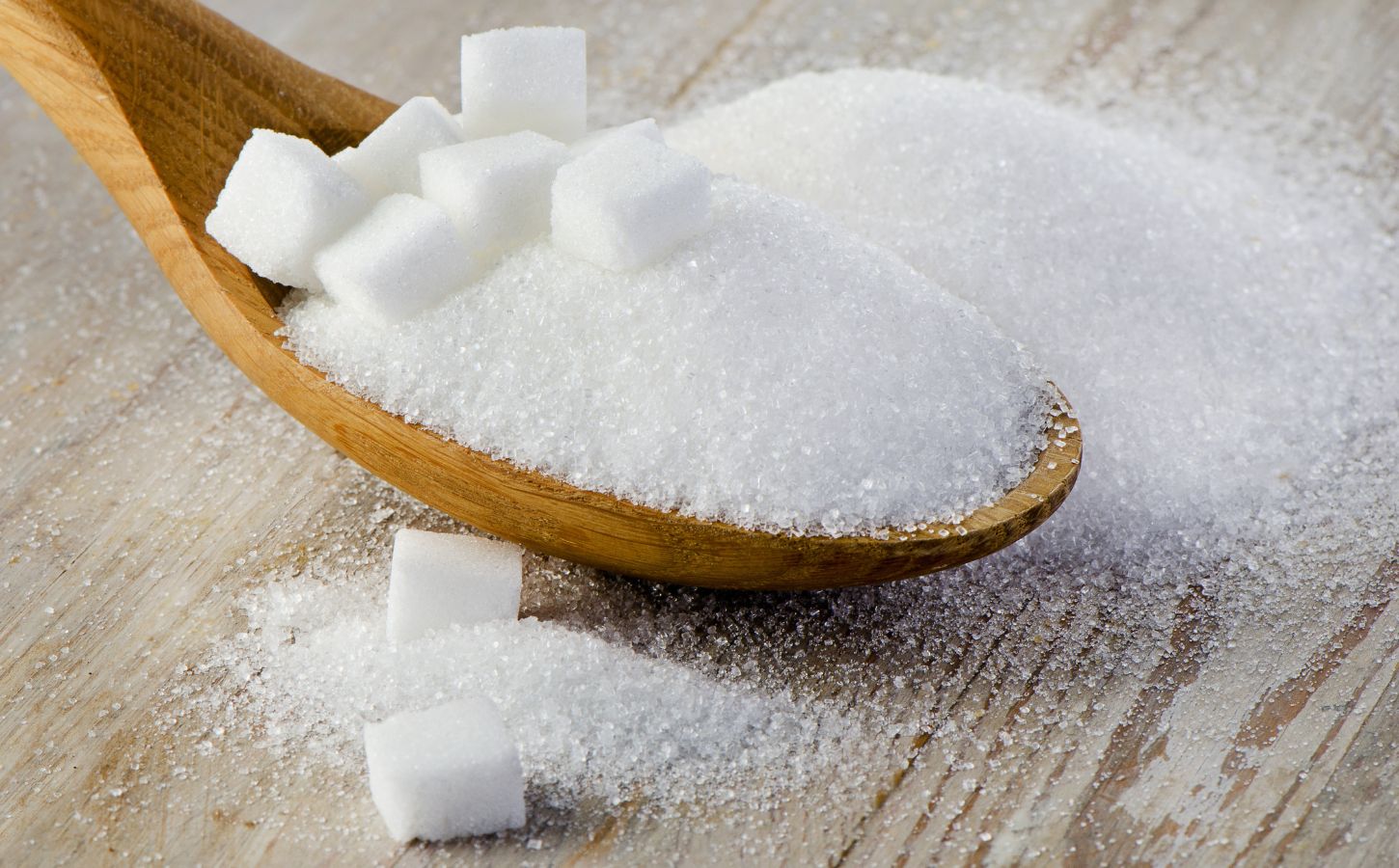 Granulated sugar and sugar cubes, which are often made from bone char, on a wooden spoon