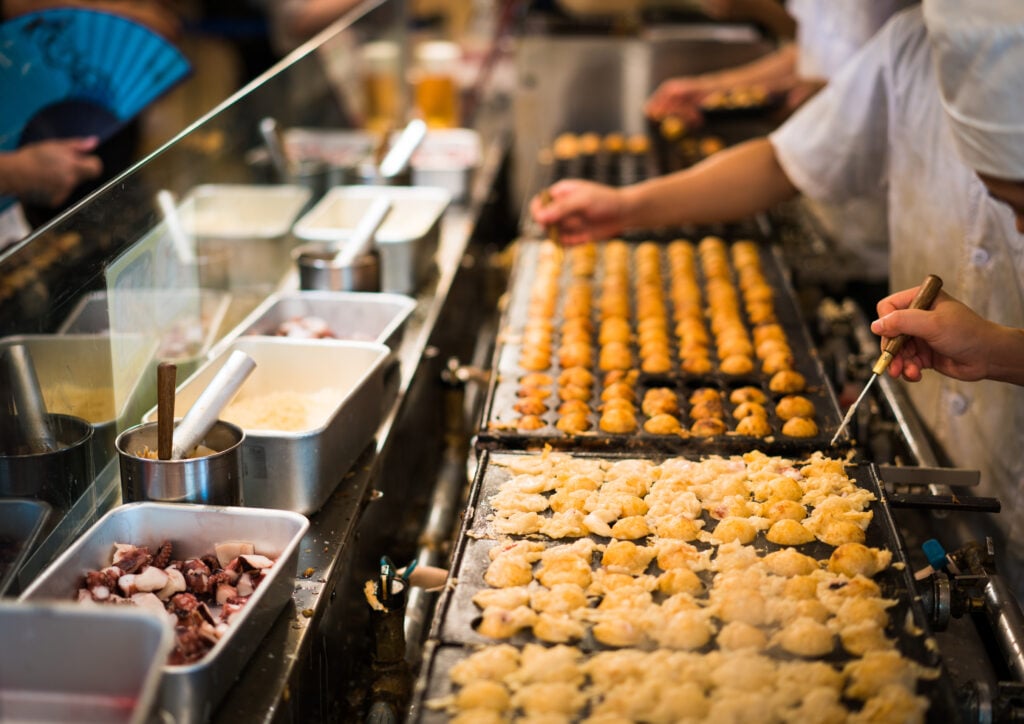 Person serving Japanese snack food “Takoyaki” shop at local market in japan
