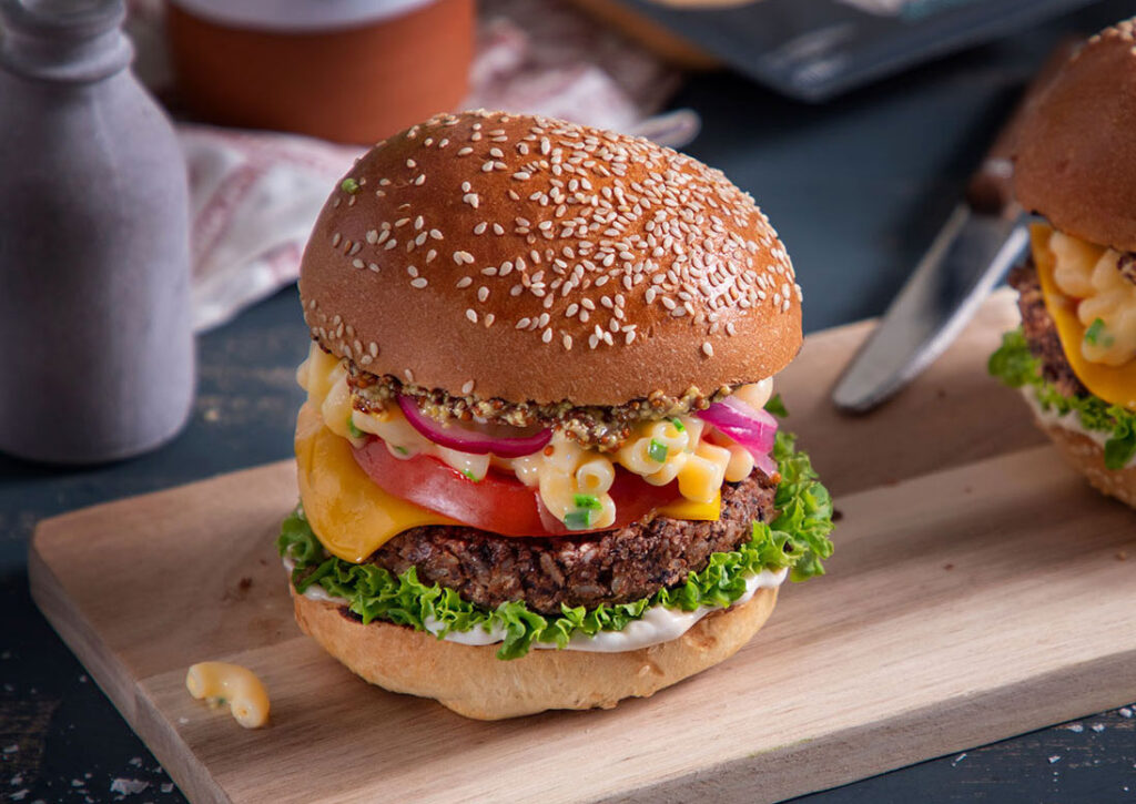 A vegan burger featuring dairy-free Violife cheese and a plant-based bean patty, resting on a chopping board