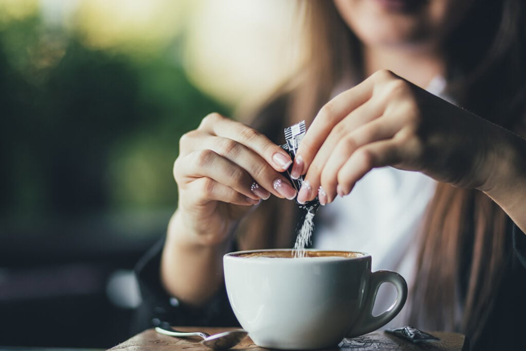 A person pouring non-vegan sugar into a coffee