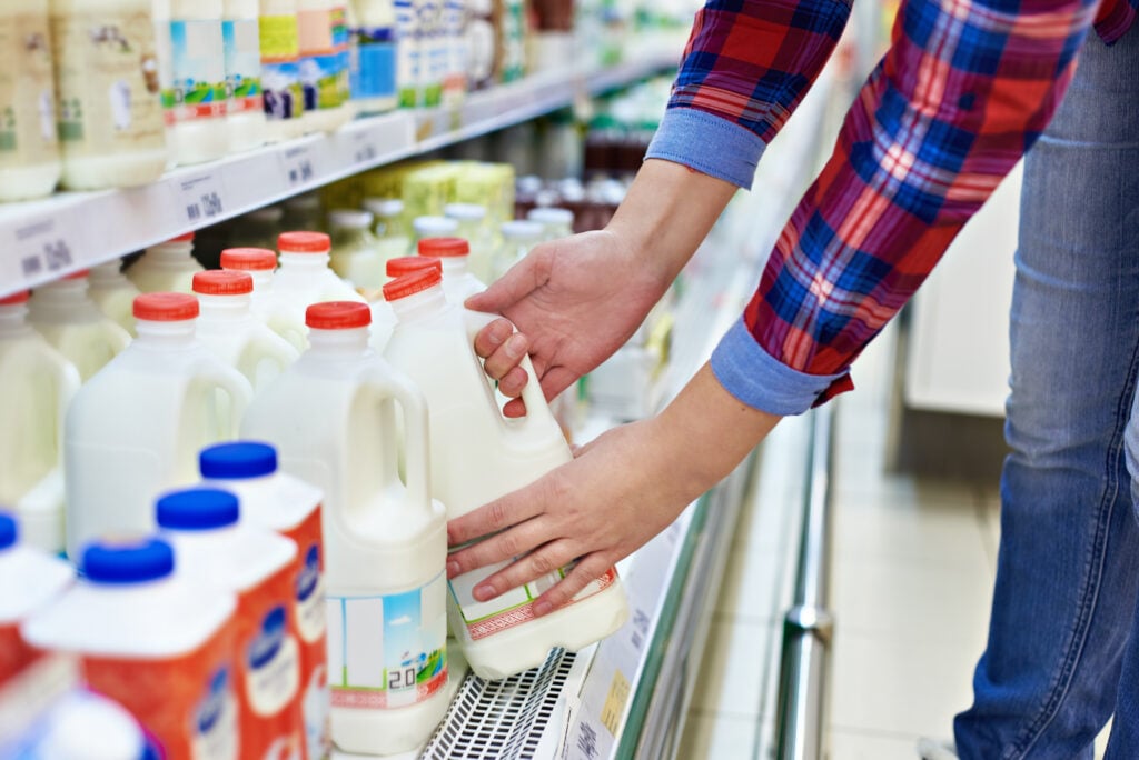 A person picking up a carton of dairy milk, which is environmentally damaging, from a supermarket shelf