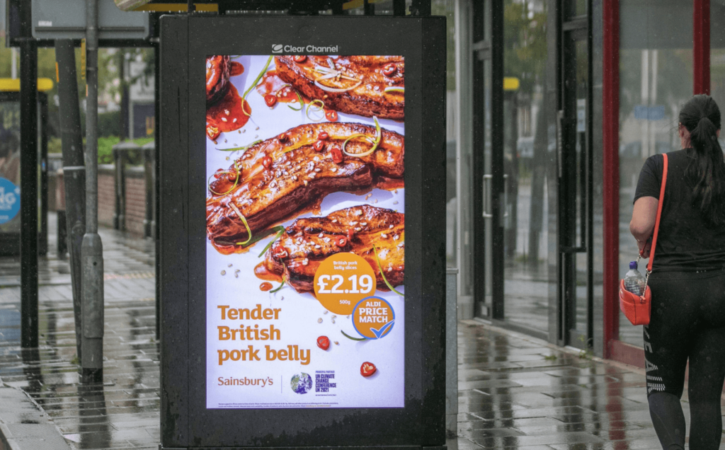 A person walking past a Sainsbury's billboard for pork in partnership with the UN Climate Change Conference UK 2021