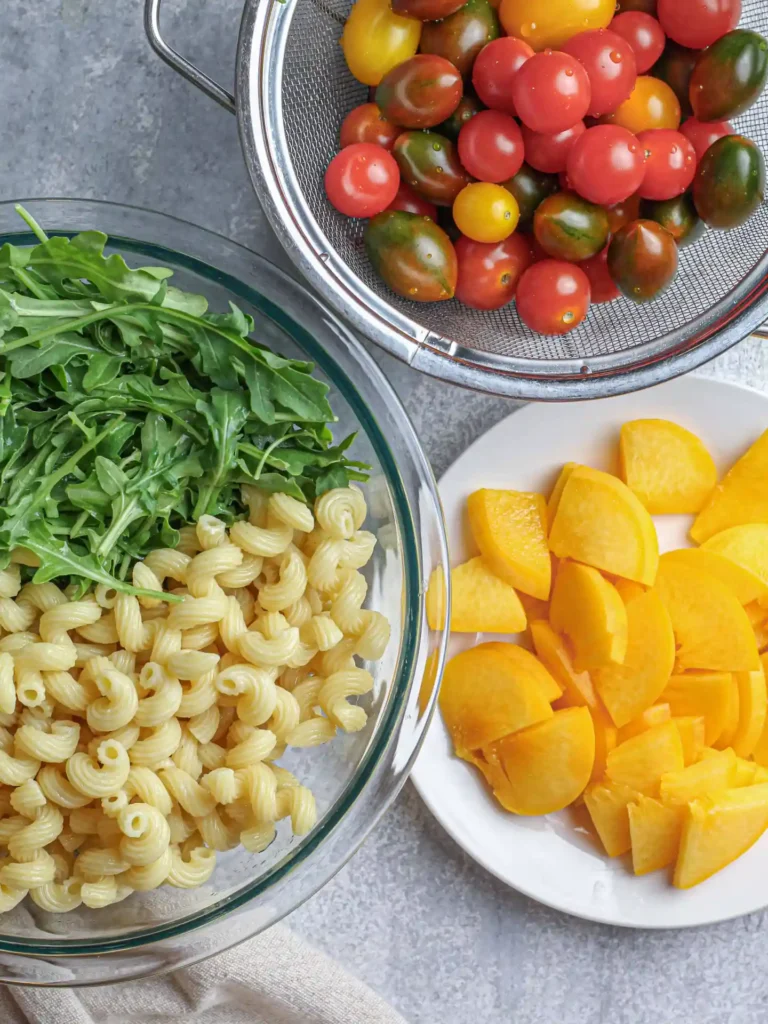 Vegan Peach Pasta Salad ingredients, including cherry tomatoes, spaghetti, watercress, and peaches