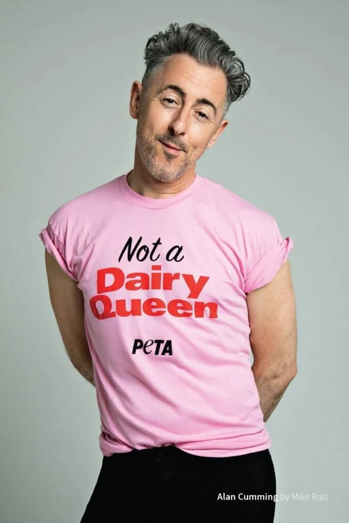 Vegan celebrity Alan Cumming poses in a pink t-shirt with the words "Not a dairy queen"