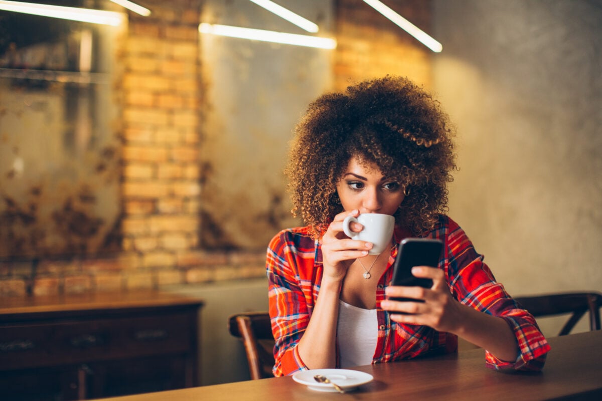 A woman drinking coffee through a vegan app on her iPhone