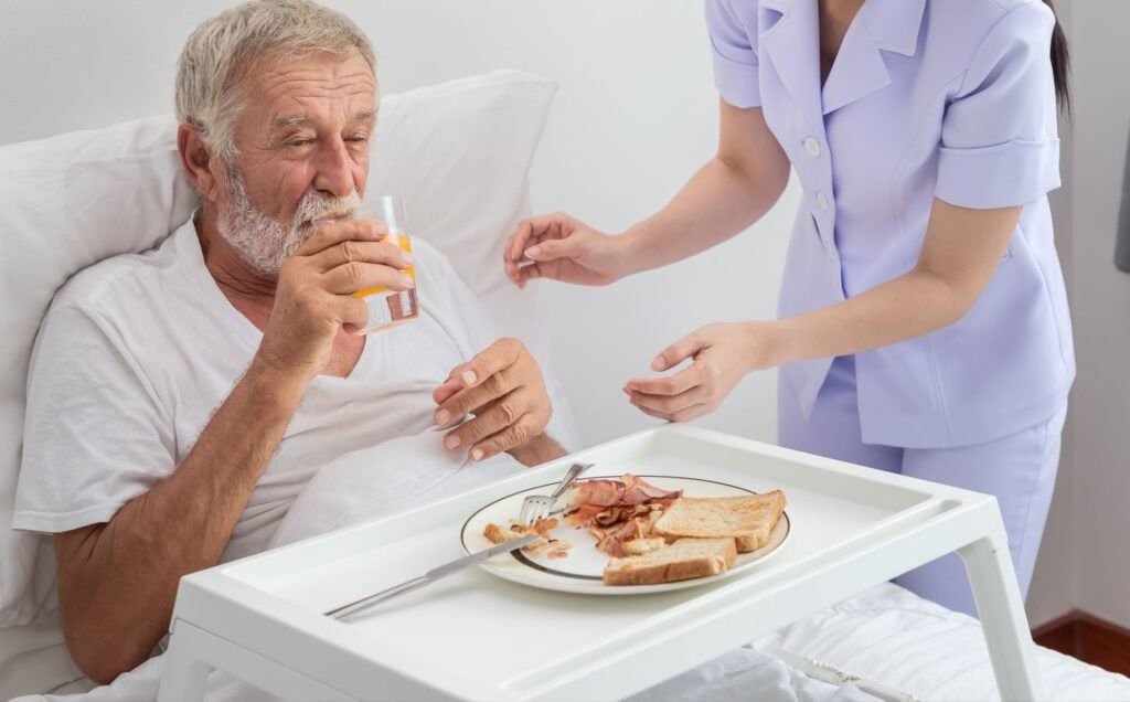 A person eating bacon, which is known to cause cancer, in a hospital bed