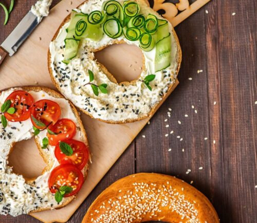 A bagel cut in half with cream cheese and tomatoes and chives