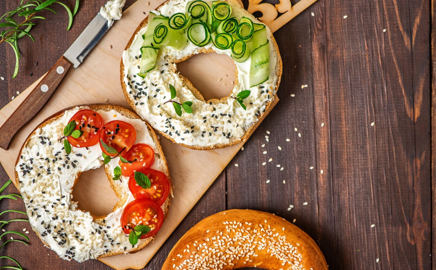 A bagel cut in half with cream cheese and tomatoes and chives