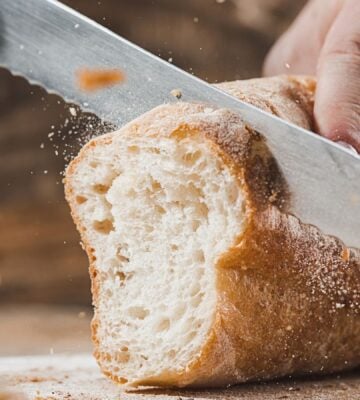 A person slicing a loaf of vegan-friendly white crusty bread