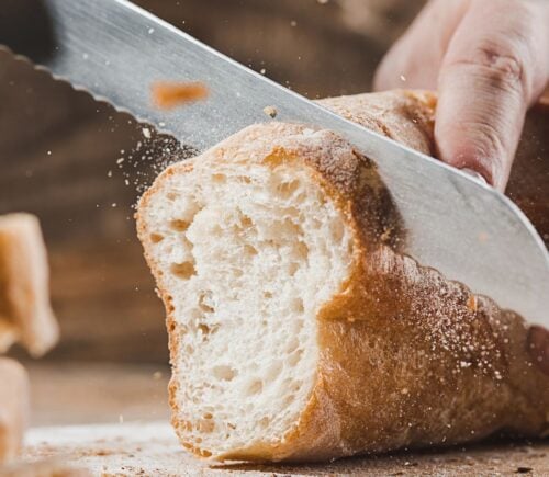 A person slicing a loaf of vegan-friendly white crusty bread
