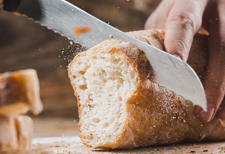 A person slicing a loaf of vegan-friendly white crusty bread