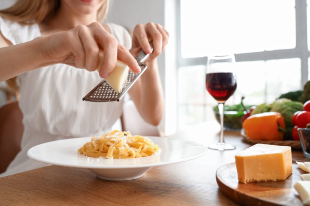 A woman grating dairy cheese onto pasta