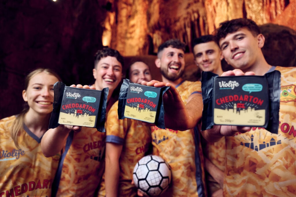 Players of Cheddar football club, which has just partnered with vegan cheese brand Violife, holding up packets of the plant-based brand's product "Cheddarton"