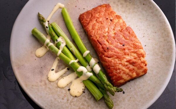 A 3D printed vegan salmon filet on a plate next to some asparagus