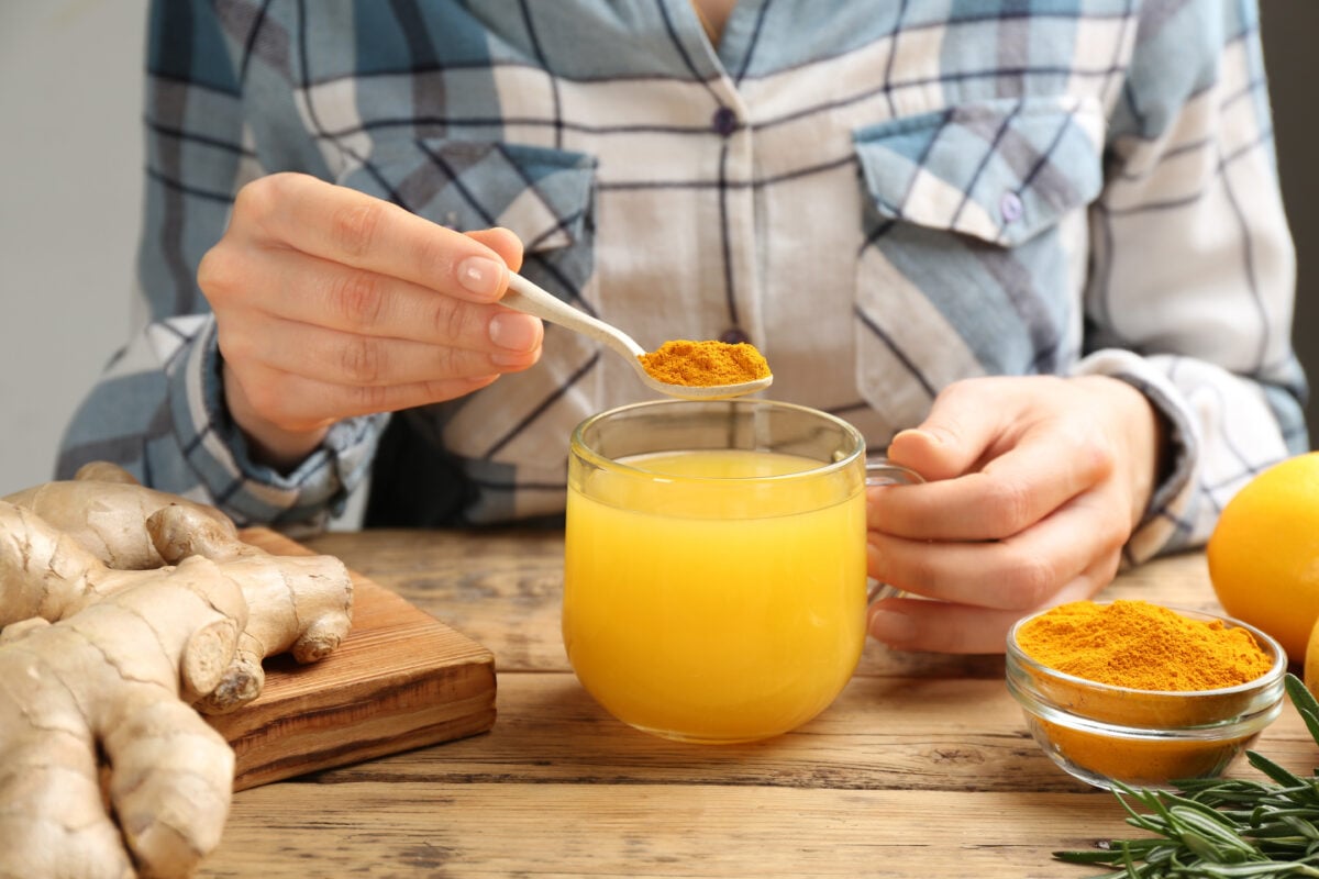 A person spooning a teaspoon of turmeric into their drink
