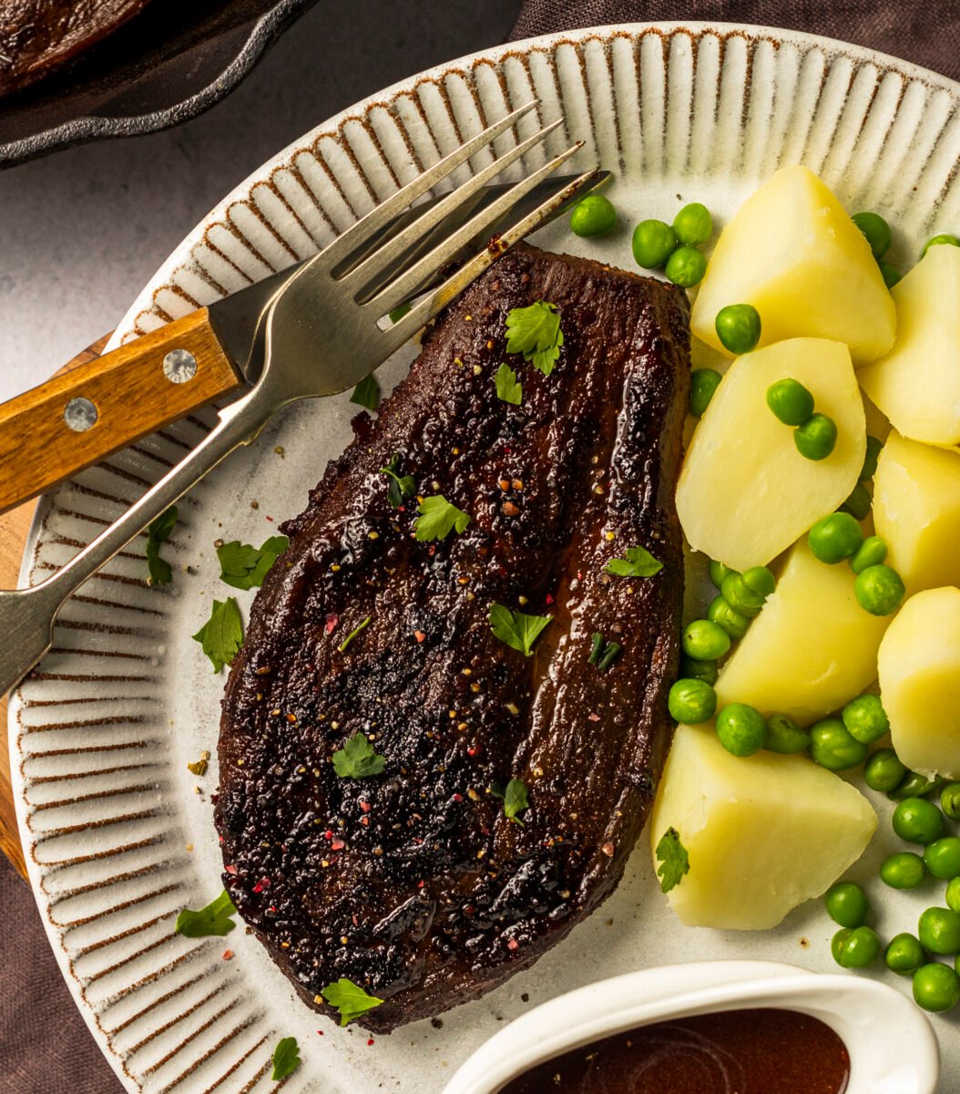 a roasted eggplant steak next to some potatoes and peas