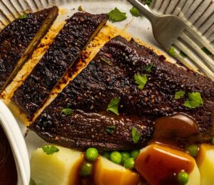 a roasted eggplant steak next to some potatoes and peas