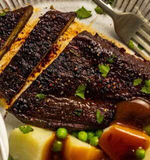 a roasted eggplant steak next to some potatoes and peas