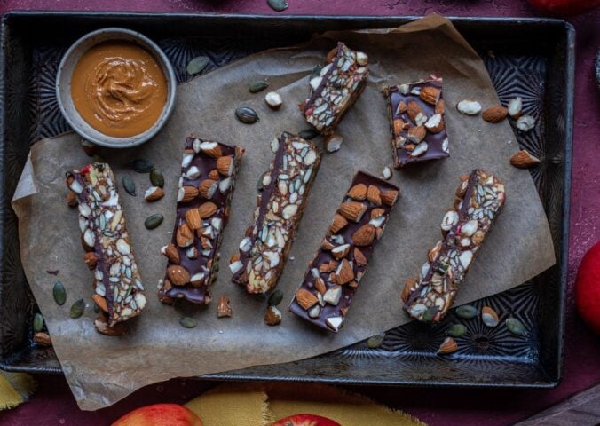 Vegan energy bars on a baking tray next to some apples and nut butter