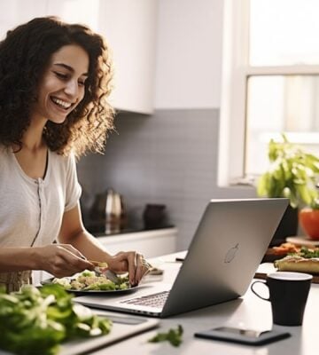 A woman smiling and cooking plant-based food while looking at her laptop