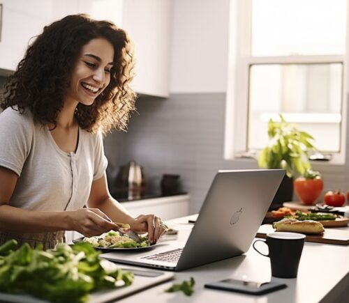 A woman smiling and cooking plant-based food while looking at her laptop