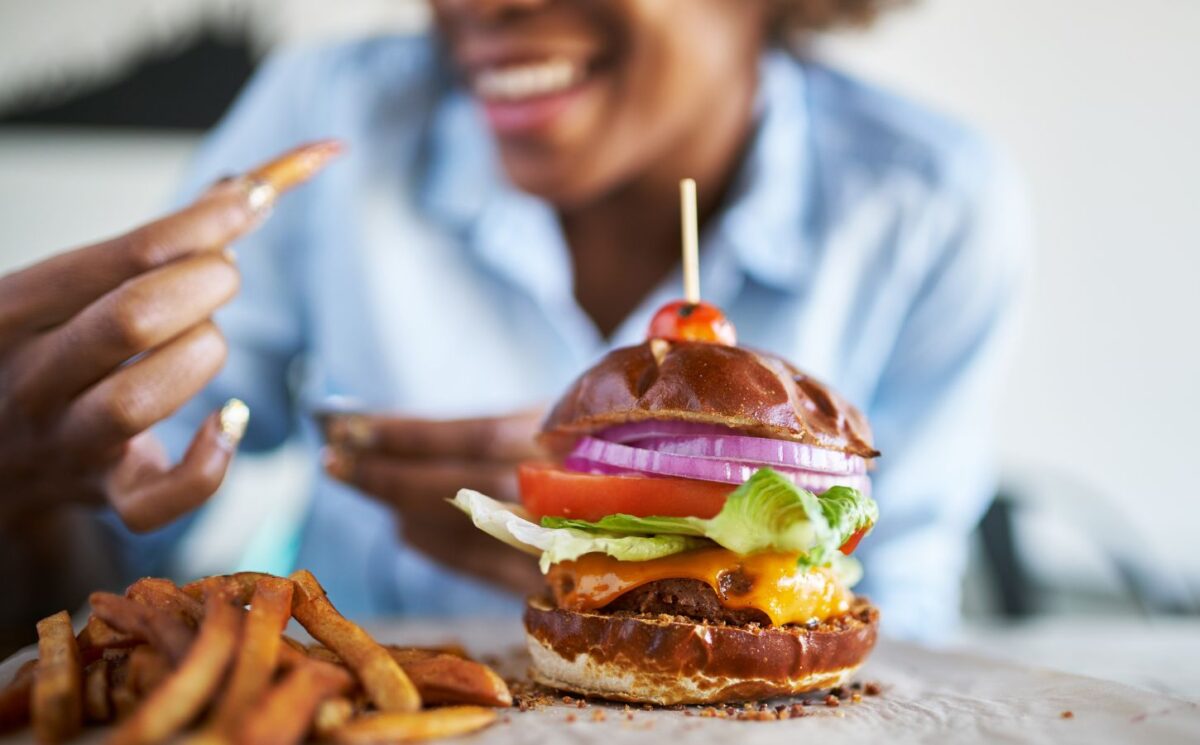 Close up of a vegan burger and chips with woman taking part in Veganuary in the background
