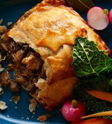 A vegan beef wellington from UK supermaret Waitrose. It's positioned on a plate next to radishes, cabbage, and carrots. the Wellington is part of Waitrose's 2023 Christmas range