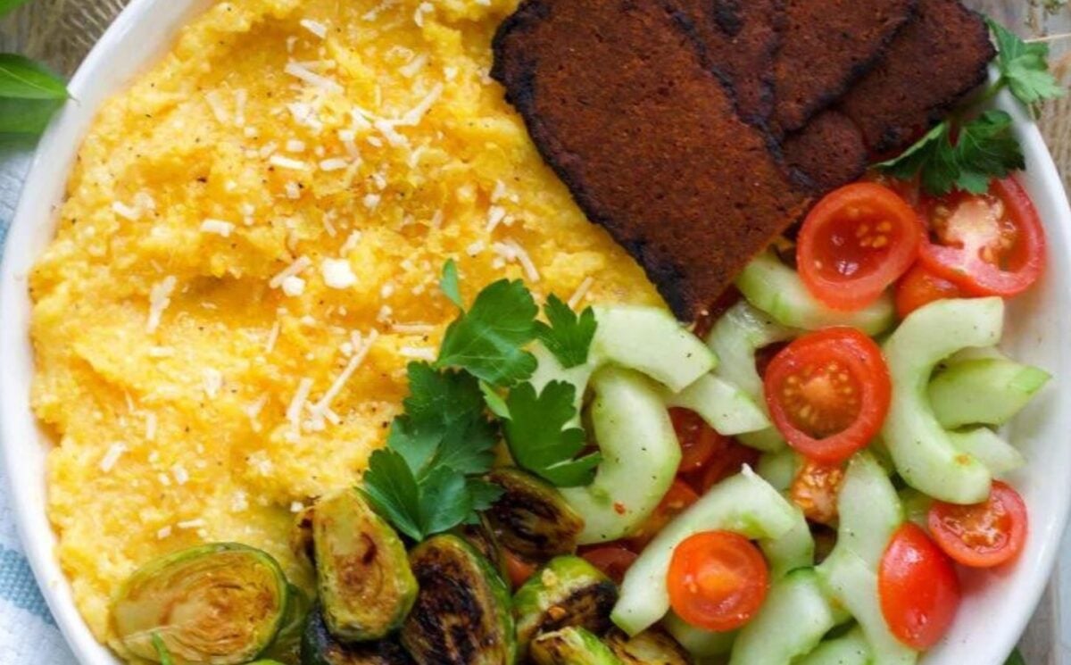 A cheesy vegan polenta breakfast bowl with dairy-free polenta, sprouds, and tomatoes and cucumber