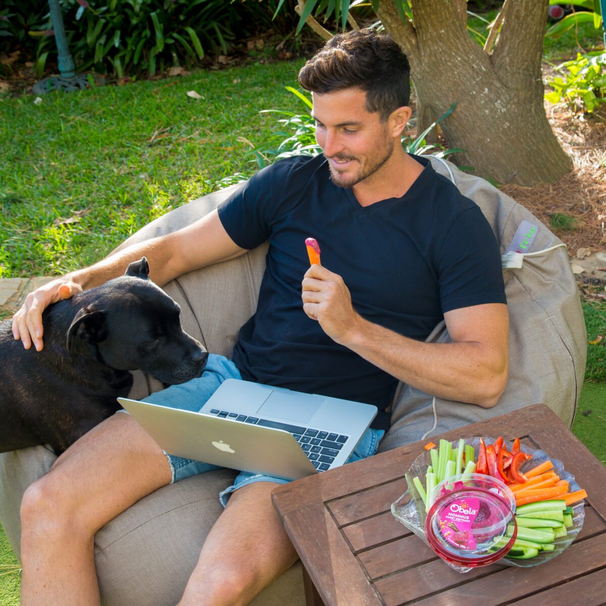 Drew Harrisberg sitting in the garden with his dog and eating a carrot stick
