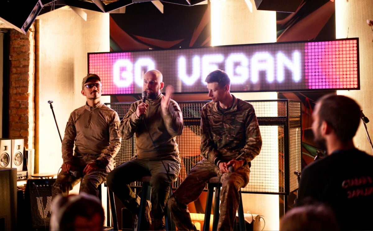 Soldiers on stage at a Ukraine vegan festival with the words "go vegan" on a screen behind them